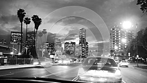 Streets of Los Angeles at night - traffic jam, moving cars, lights, palm trees and skyscrapers building - all in black and white
