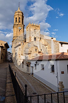 Streets of the medieval town of La Iglesuela del Cid with the Church of Purification in the background on a blue day with clouds,