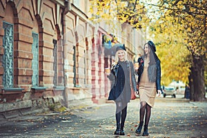 Streetstyle and fashion! Outdoors shot of young women with coffee on city street. Two fashion girls walking outdoor with cofee.