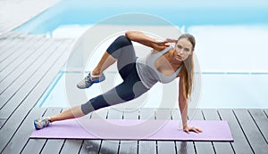 Strength and focus. Shot of a gorgeous young woman doing yoga outdoors beside a pool.