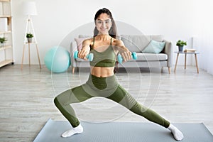 Strength training concept. Athletic Indian woman doing exercises with dumbbells indoors, full length