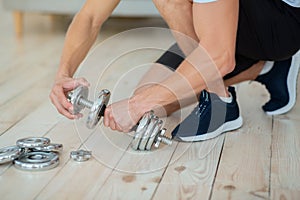 Strength training at home. Man puts discs on dumbbells for workout