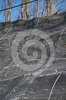 Strengthening the mountain slope with a metal mesh that prevents rockfall on the road. Abstract background of the
