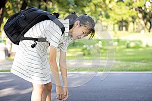 Stress asian child girl carrying heavy school bag or backpack, female teenage feeling pain on back, full of books on her back,