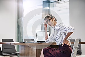 Stress, bad for her back and bad for business. a young businesswoman experiencing back pain while working in an office.