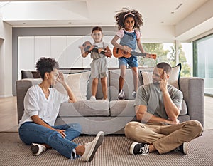 Stress, family and energy with kids playing music on a guitar in the living room at home while giving mom and dad a