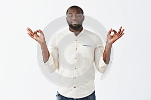 Stress floats away with every minute during meditation. Happy relieved dark-skinned calm man with beard in casual outfit