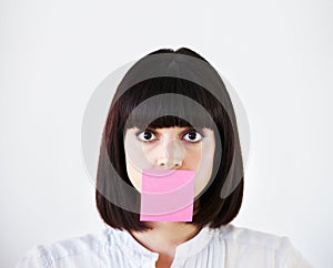 Stress is stifling her creative voice. Conceptual image of a young businesswoman with a pink post-it note covering her