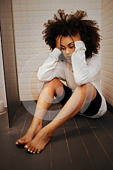 Stress, tired and mental health with young black woman sitting on bathroom floor of shower at home. Headache, depression