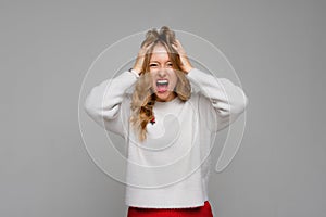 Stress. Woman stressed is going crazy pulling her hair in frustration and shouting from regret. Young emotional woman, wears white