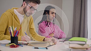 Stressed African American girl closing laptop and crossing hands as her male Caucasian groupmate in eyeglasses rolling