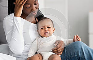 Stressed African American mom sitting with kid on bed