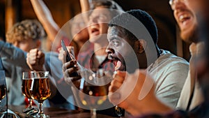 Stressed African Man Watching a Live Soccer Match on TV in a Sports Bar. Excited Fans Cheering and