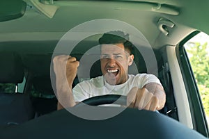 Stressed angry man in driver`s seat of modern car, view through windshield