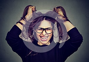 Stressed angry woman pulling hair out screaming on gray wall background