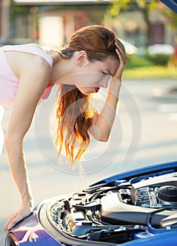 Stressed, angry young woman in front of her broken down car