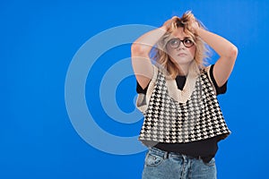 Stressed and anxious caucasian young woman with her arms up. Angry look. Blue background studio shot.