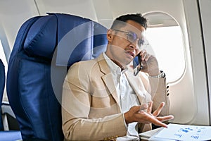 Stressed Asian businessman is having a serious conversation on the phone during his flight