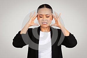 Stressed Asian businesswoman with a pained expression, holding her head in frustration or headache