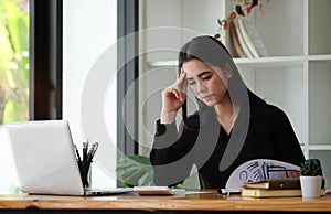 Stressed asian businesswoman sitting at office desk and checking financial documents