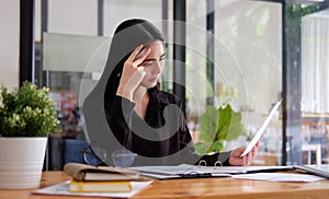 Stressed asian businesswoman sitting at office desk and checking financial documents