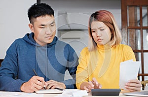 Stressed Asian couple serious calculate home financial bill budget on table in kitchen at new house