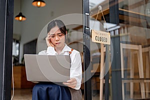 A stressed Asian female coffee shop owner looking at a laptop screen with a serious and sad face