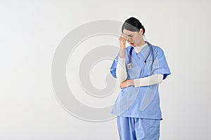 A stressed Asian female doctor in scrubs suffering from headaches or migraines