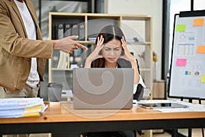 Stressed Asian female office employee getting complaint by her boss, feeling tired of work