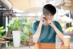 A stressed Asian man talking on the phone while sitting at an outdoor table of a cafe in the city