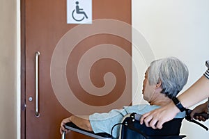 Stressed asian senior woman with wheelchair waiting on a long time at front disabled toilet,queue of disabled elderly waiting at