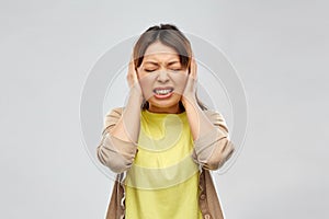 Stressed asian woman closing ears by hands