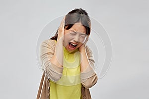 Stressed asian woman closing ears and screaming