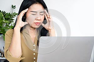 Stressed Asian woman having headache, migraine at work tired from working on computer hand touching her head