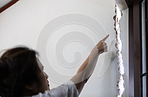 Stressed asian woman is pointing at the cracks,rift of wall in her house,collapsed after repair or extension of substandard