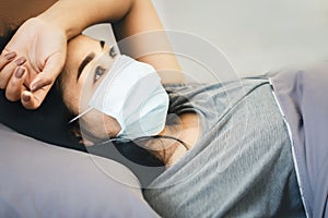 stressed Asian woman with protective face mask lying down in bed thinking or worry of sickness