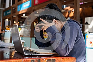 A stressed Asian woman is working on her project on her laptop, facing issues with her work