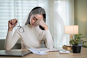 A stressed Asian woman is worried about financial problems while sitting at a table