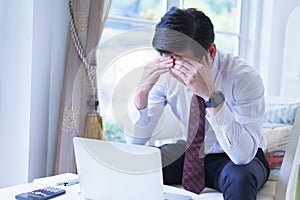 Stressed asian young businessman working with laptop and holding head with hands looking down.