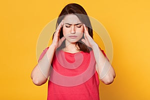 Stressed beautiful woman wears casual t shirt, touching temples and has terrible headache, attractive young lady looks tired.