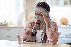 Stressed Black Lady Taking Painkiller Pill While Sitting At Table In Kitchen