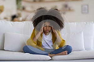 Stressed black little girl sitting on couch at home