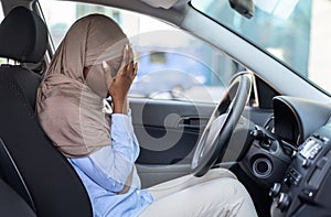 Stressed black muslim woman driver sitting in car, covering face with hands