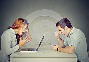 Stressed business woman with laptop sitting at table with angry man screaming at mobile phone. Negative emotions in office life