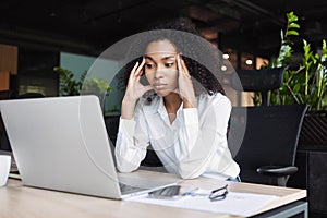 Stressed business woman sitting at office workplace looking at laptop computer. Tired and overworked businesswoman has headache