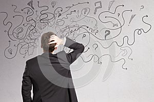 Stressed businessman with abstract arrows sketch on concrete wall background.