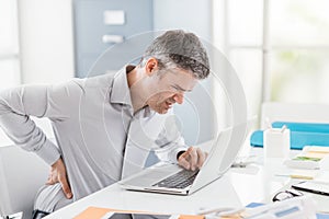 Stressed businessman with backache, he is working at office desk and massaging his back