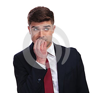 Stressed businessman biting his nails looks up to side