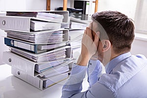 Stressed Businessman In Front Of Stacked Folders