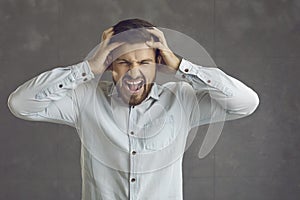 Portrait of a stressed angry young man screaming standing on a gray studio background